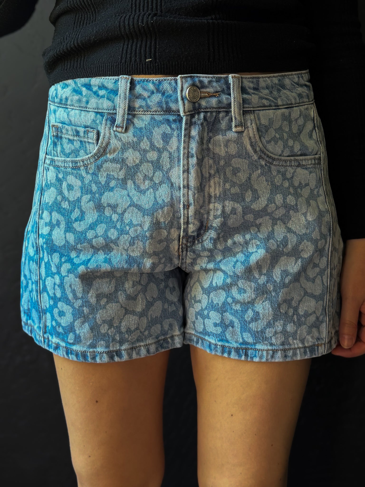 Blue leopard print denim shorts worn by a person on a black background