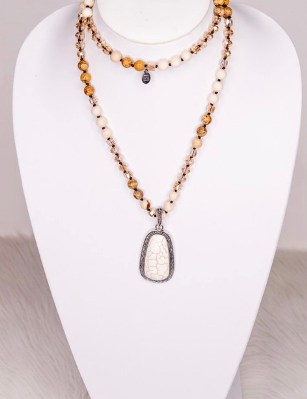 A beaded strand necklace with crystal and stone beads, featuring a unique stone pendant, displayed on a mannequin bust.