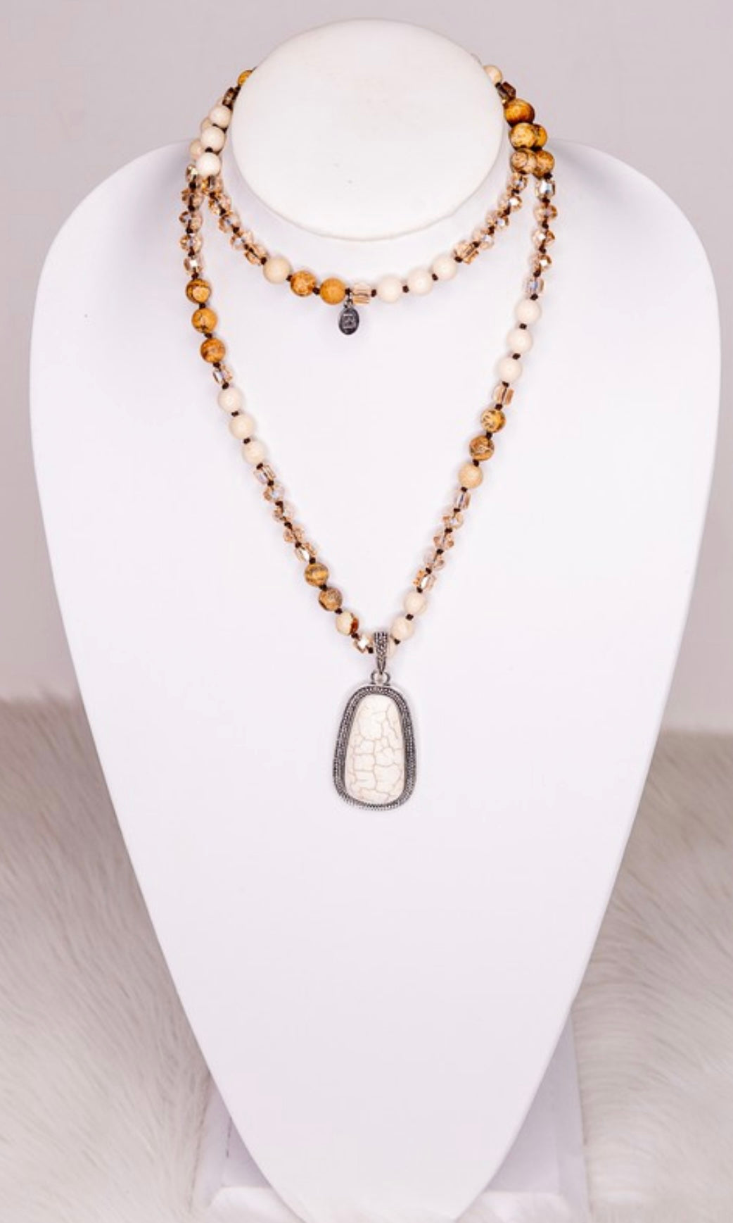A beaded strand necklace with crystal and stone beads, featuring a unique stone pendant, displayed on a mannequin bust.