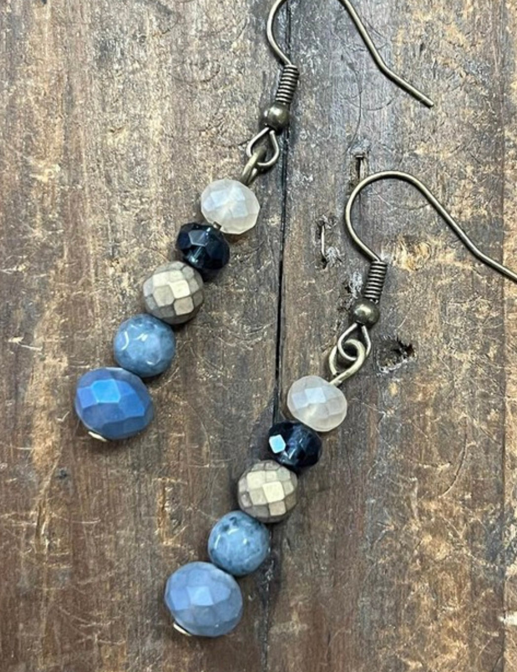 A pair of fishhook dangle earrings with denim blue crystal beads, displayed against a wooden background.