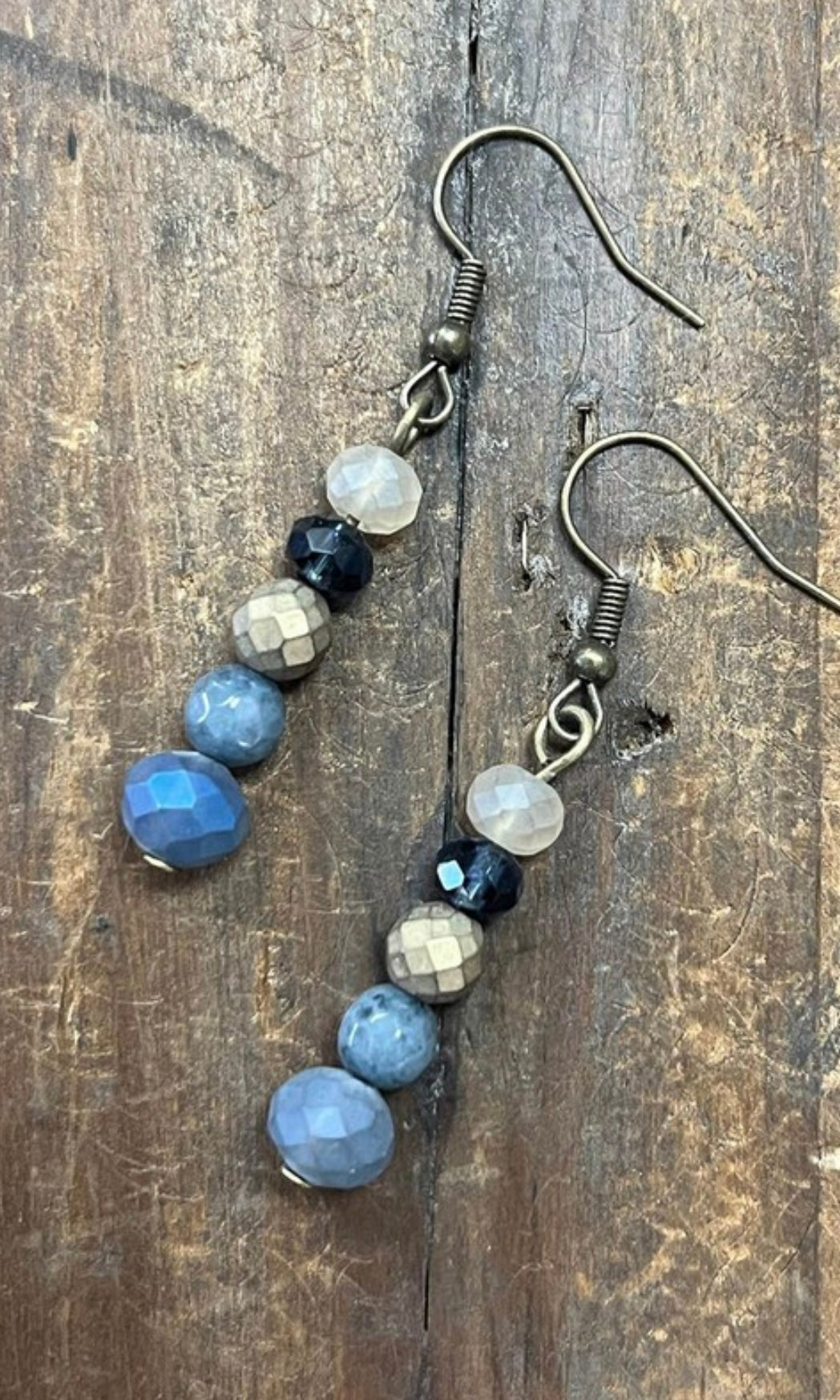 A pair of fishhook dangle earrings with denim blue crystal beads, displayed against a wooden background.