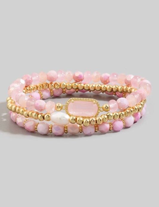 Set of pink beaded bracelets with gold accents on a light gray background