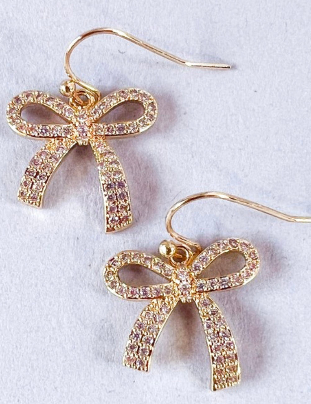 A pair of small rhinestone bow earrings attached to fishhook earrings, displayed against a white background.