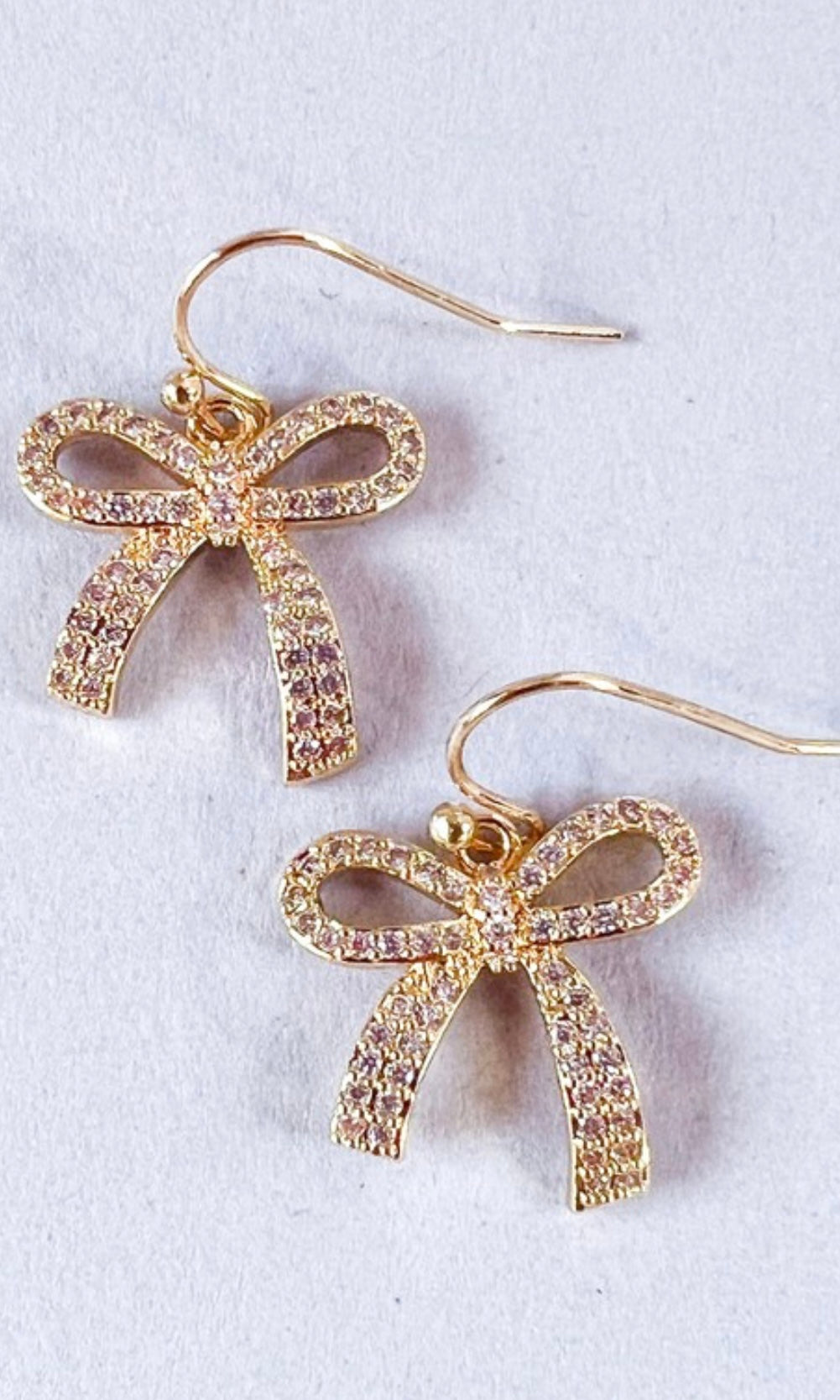 A pair of small rhinestone bow earrings attached to fishhook earrings, displayed against a white background.