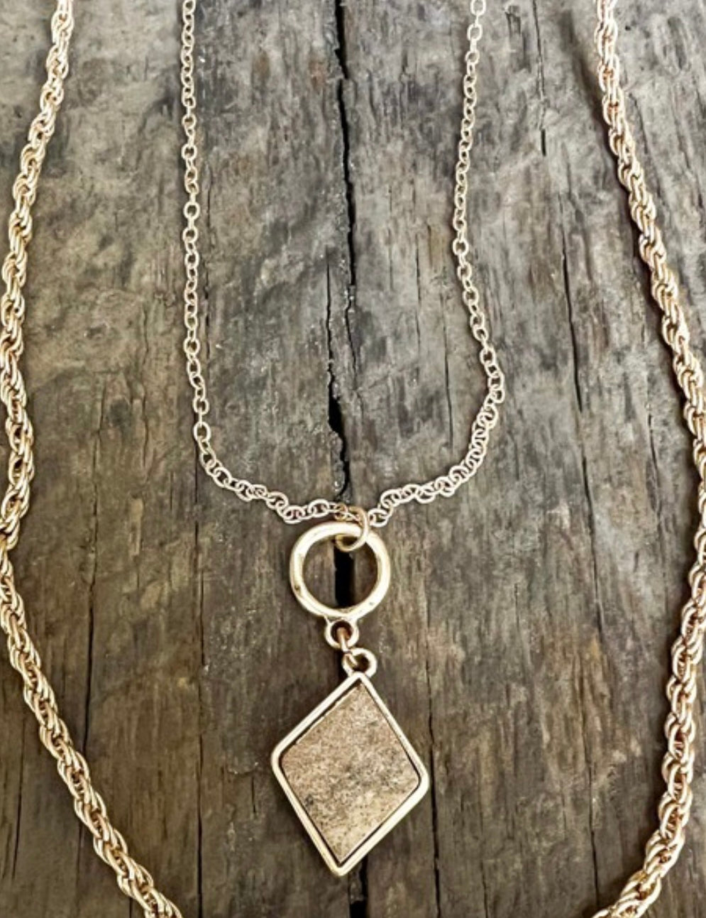 Two necklaces, one with a rope chain and the other with a cable chain, both featuring a diamond-shaped pendant, displayed against a wooden background.