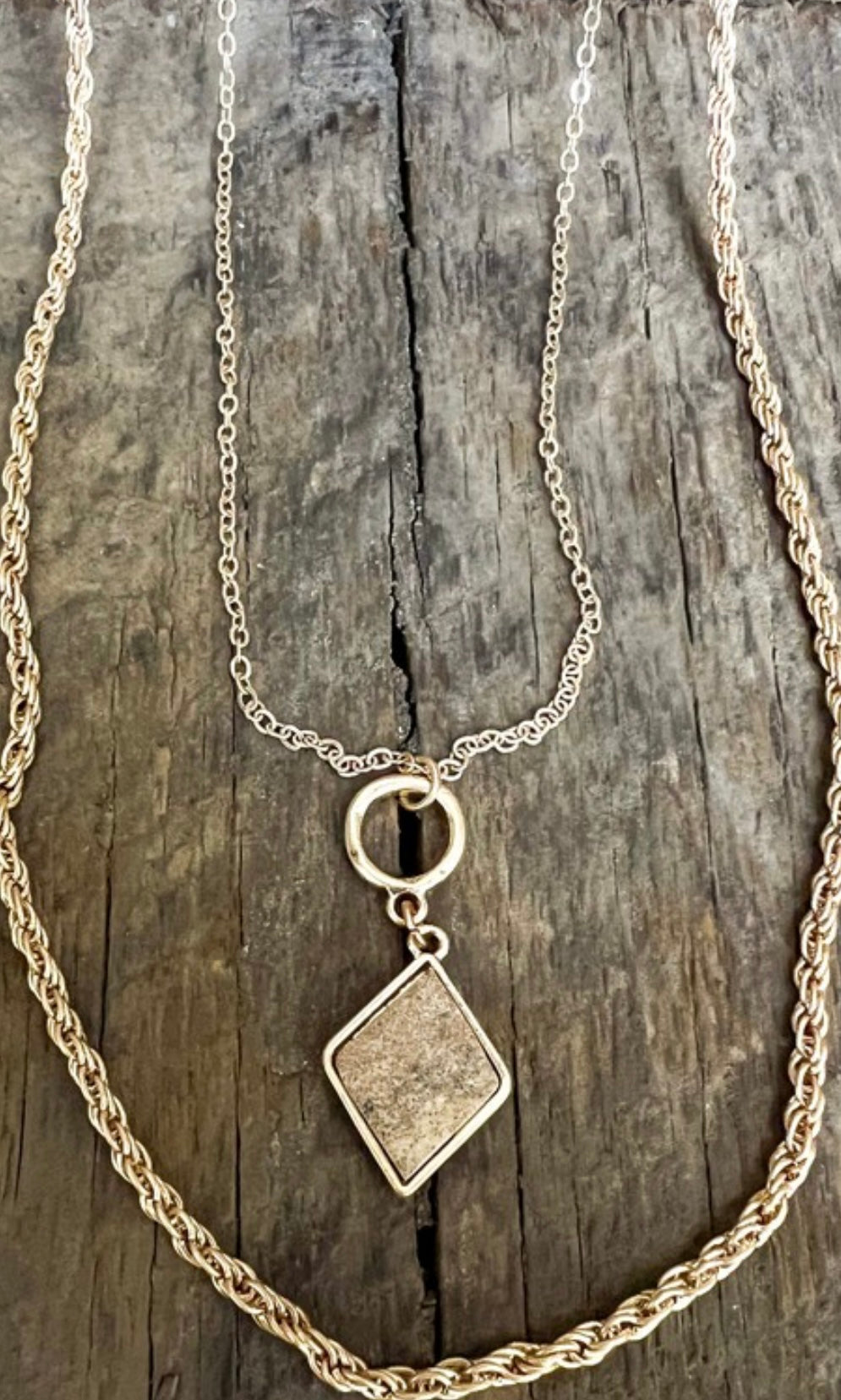 Two necklaces, one with a rope chain and the other with a cable chain, both featuring a diamond-shaped pendant, displayed against a wooden background.