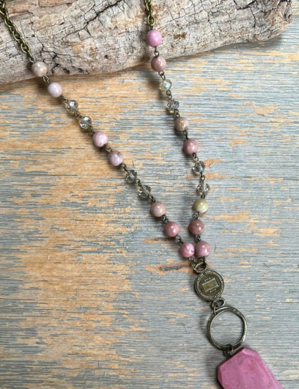 A long chain necklace with multicolored beads and a pink polished agate pendant, displayed on a wooden surface.