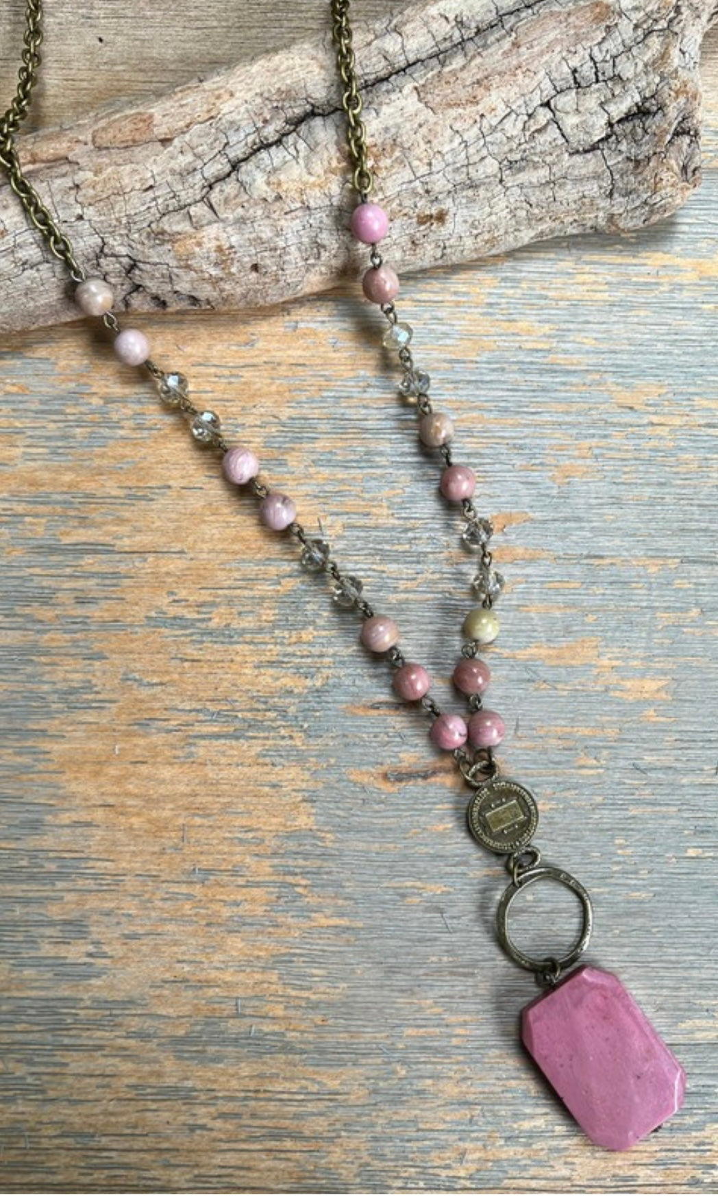 A long chain necklace with multicolored beads and a pink polished agate pendant, displayed on a wooden surface.
