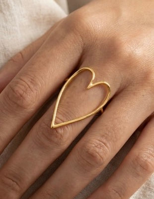 Gold heart-shaped ring on a person's finger with a neutral background