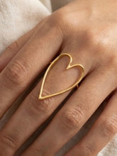 Gold heart-shaped ring on a person's finger with a neutral background