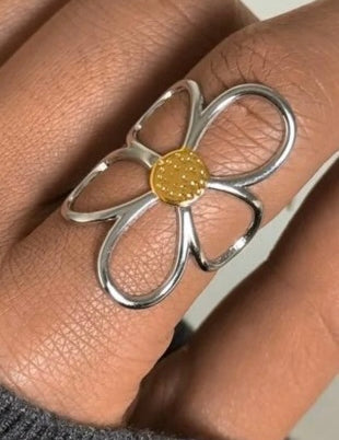Silver flower-shaped ring with a gold center on a finger