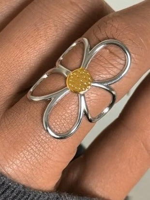 Silver flower-shaped ring with a gold center on a finger