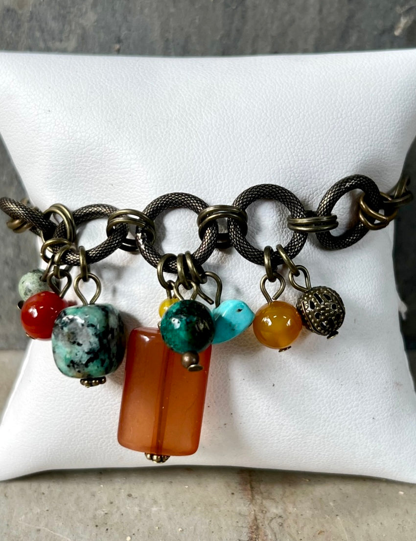 A multicolored beaded bracelet with a bronze chain link and lobster clasp, displayed on a white card.