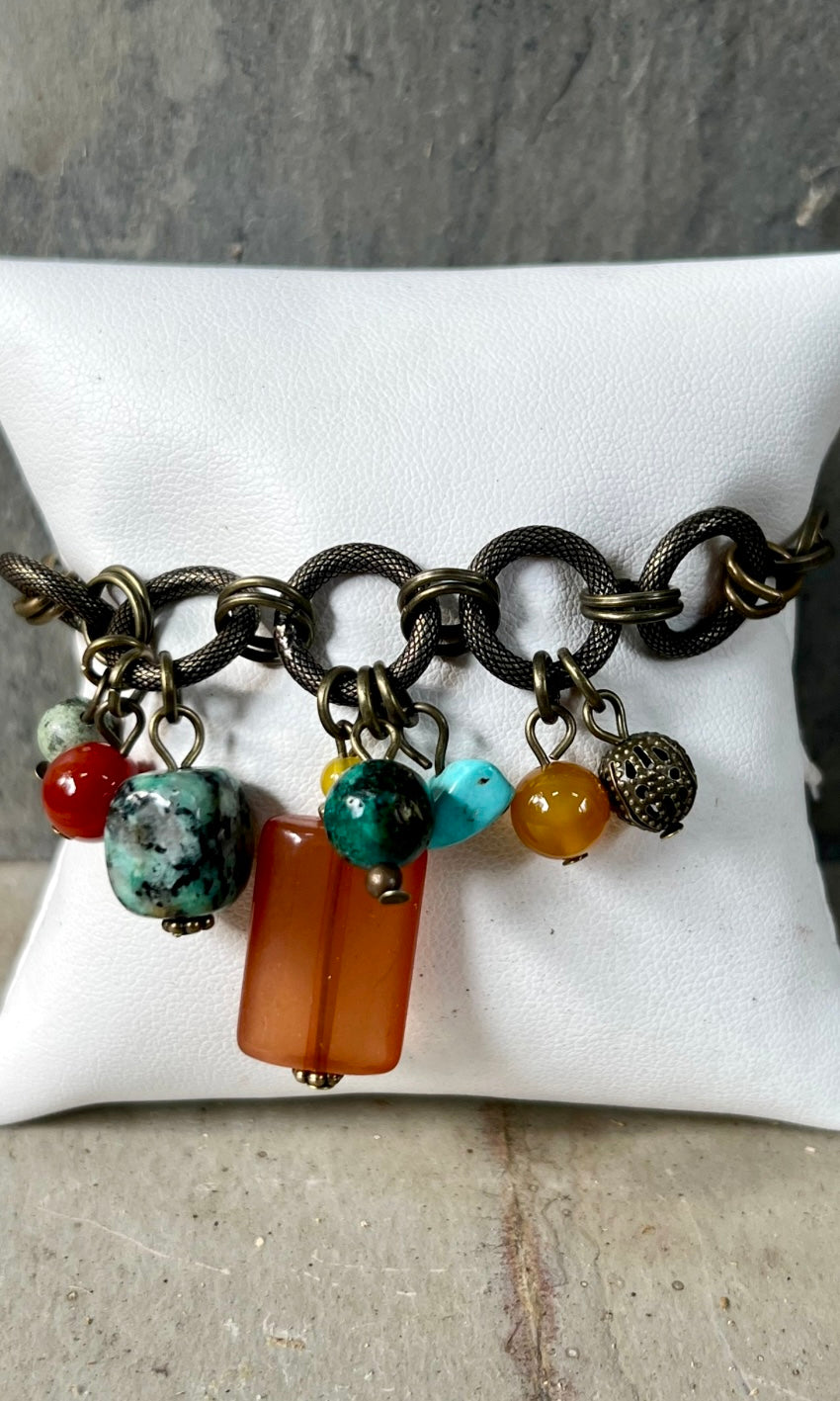 A multicolored beaded bracelet with a bronze chain link and lobster clasp, displayed on a white card.