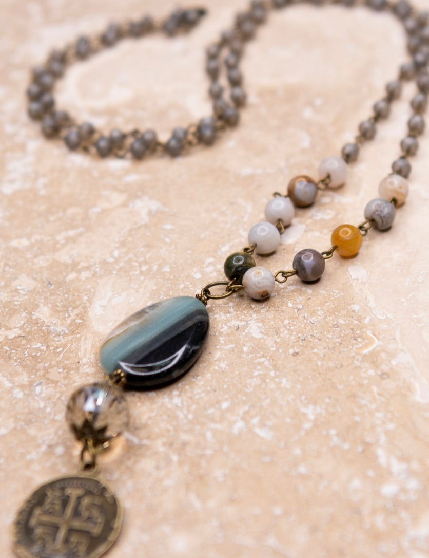 A long beaded chain link necklace with a grey stone pendant and a metal doubloon coin pendant.