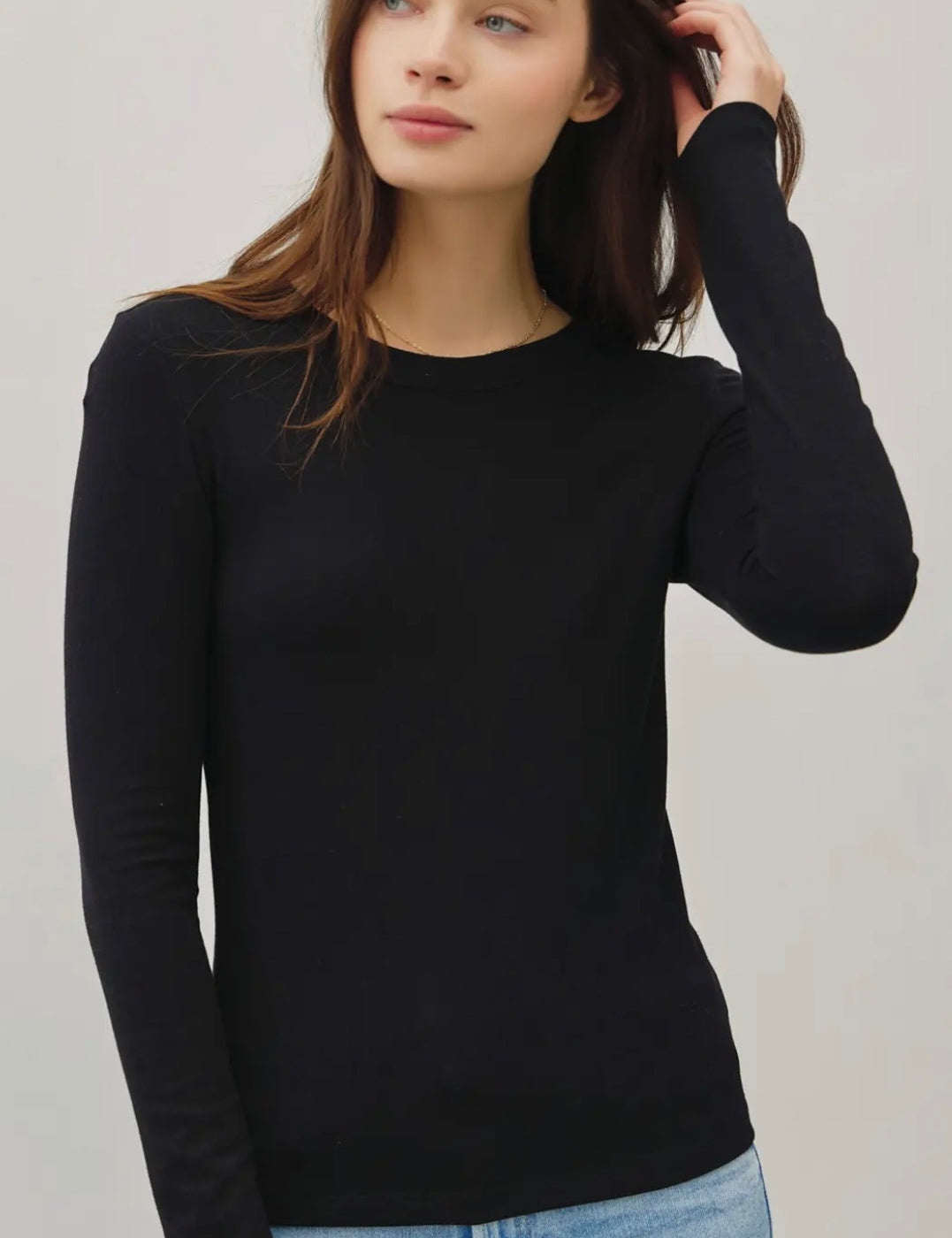 Woman wearing a black long-sleeve top and blue jeans against a plain background