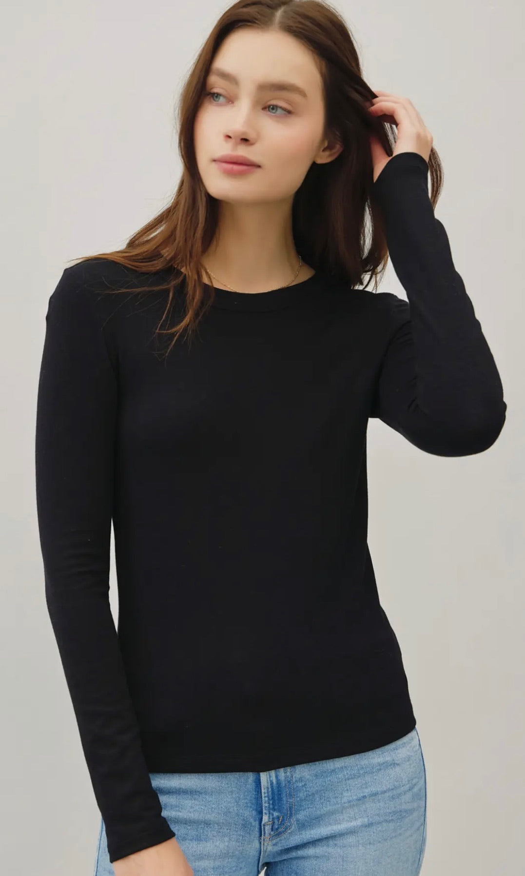 Woman wearing a black long-sleeve top and blue jeans against a plain background