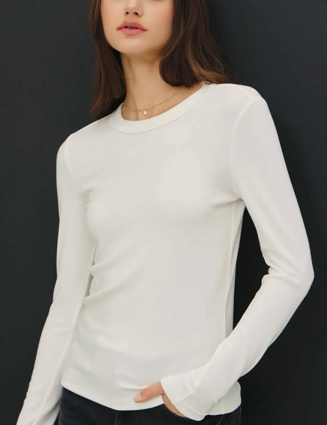 Woman wearing a white long-sleeve top against a black background
