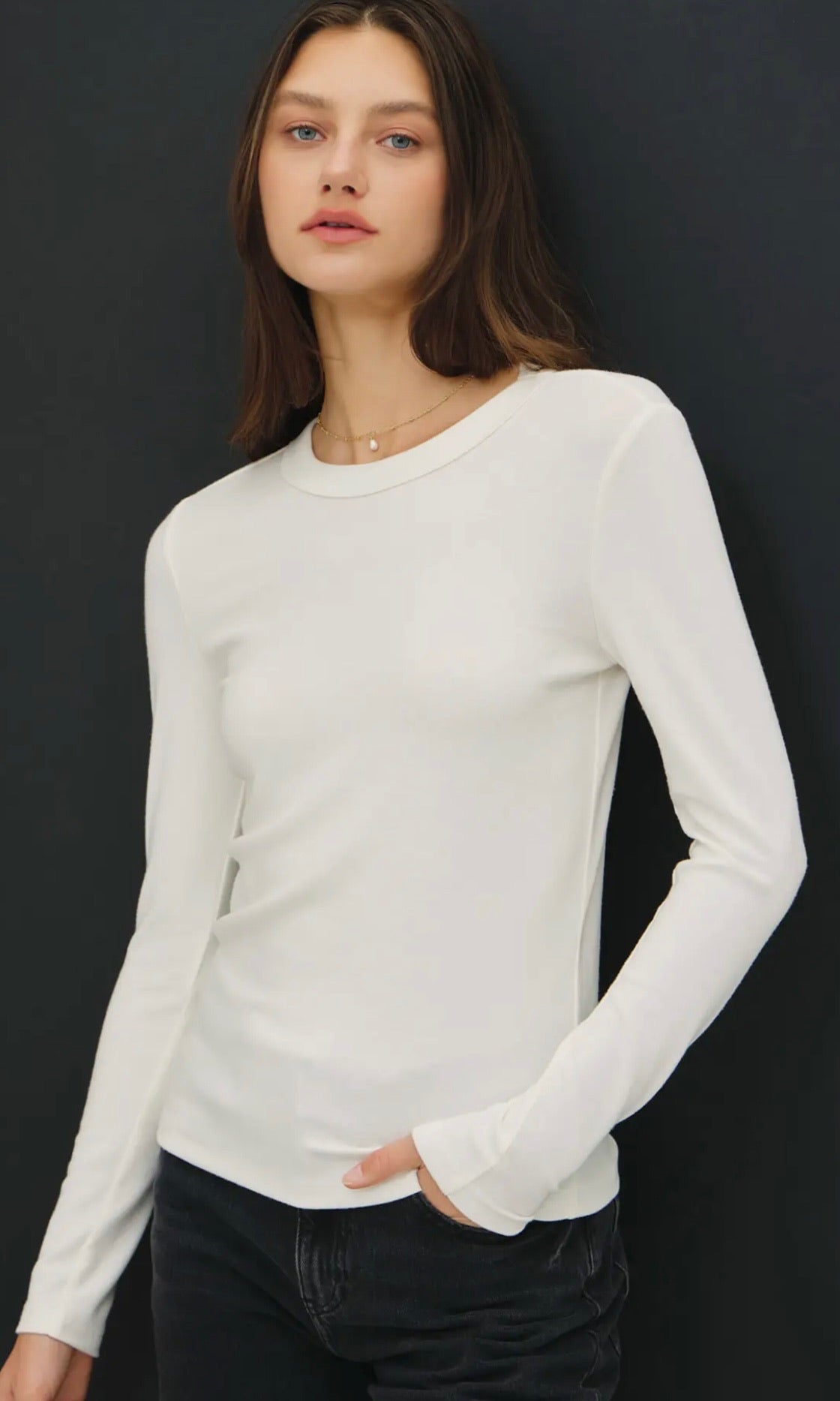 Woman wearing a white long-sleeve top against a black background