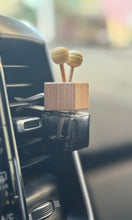 Car air freshener with wooden top and clear base attached to a car's ventilation system.