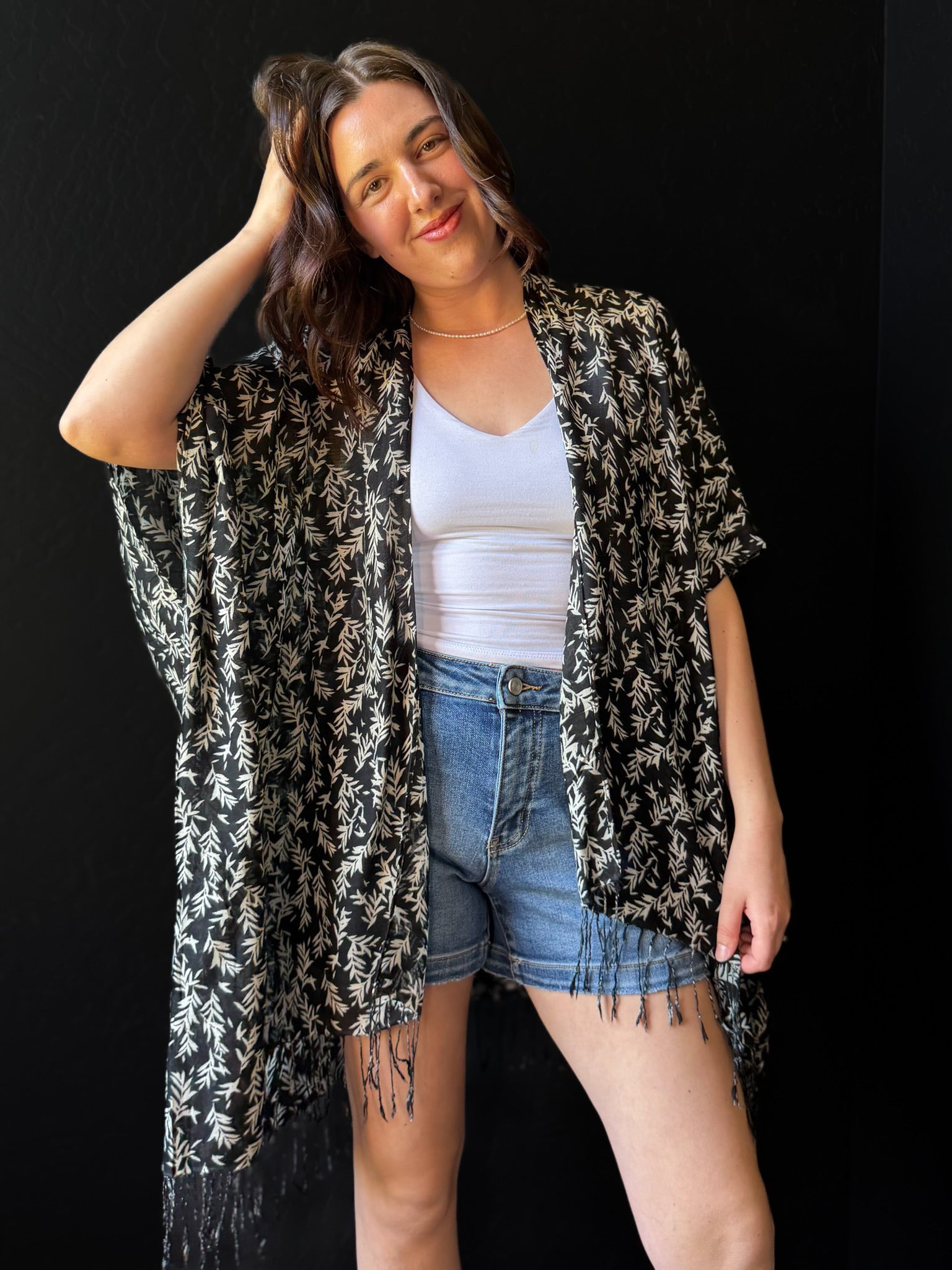 Woman wearing a black and white patterned kimono over a white top and denim shorts on a black background
