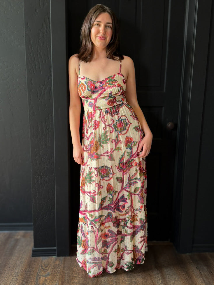 Woman wearing a floral dress standing against a dark paneled wall.
