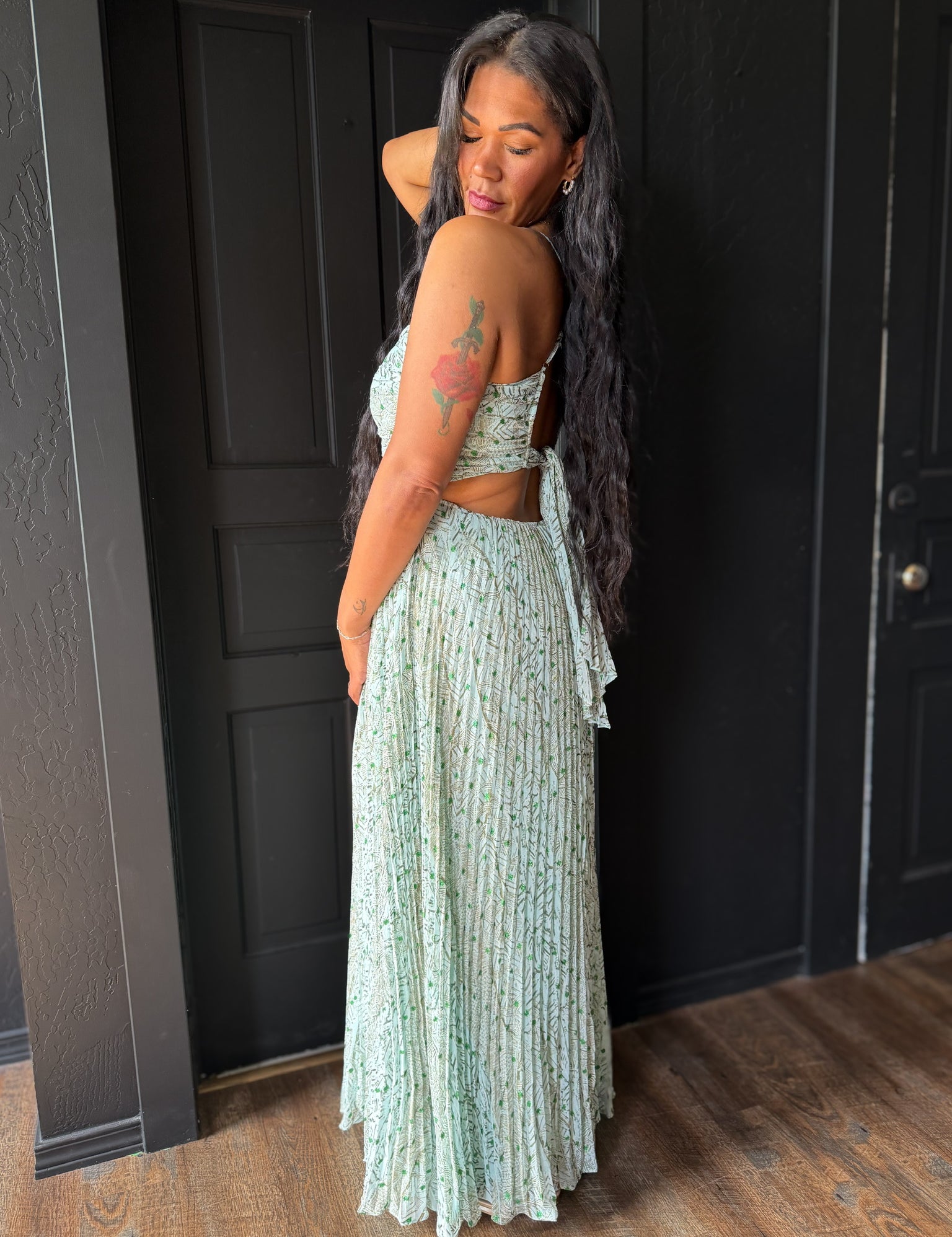 Woman in a light green floral dress standing against a dark paneled wall.
