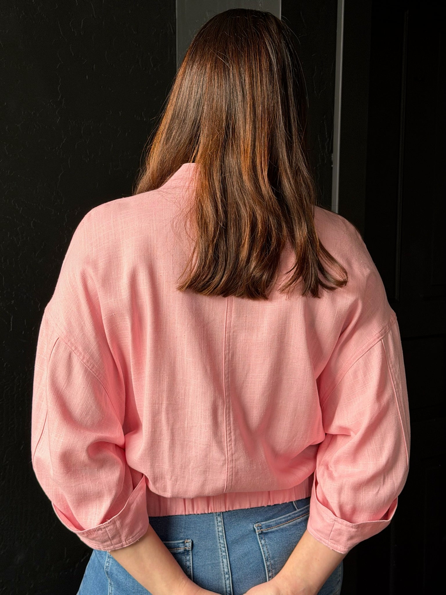 Person wearing a pink jacket and blue jeans against a dark background