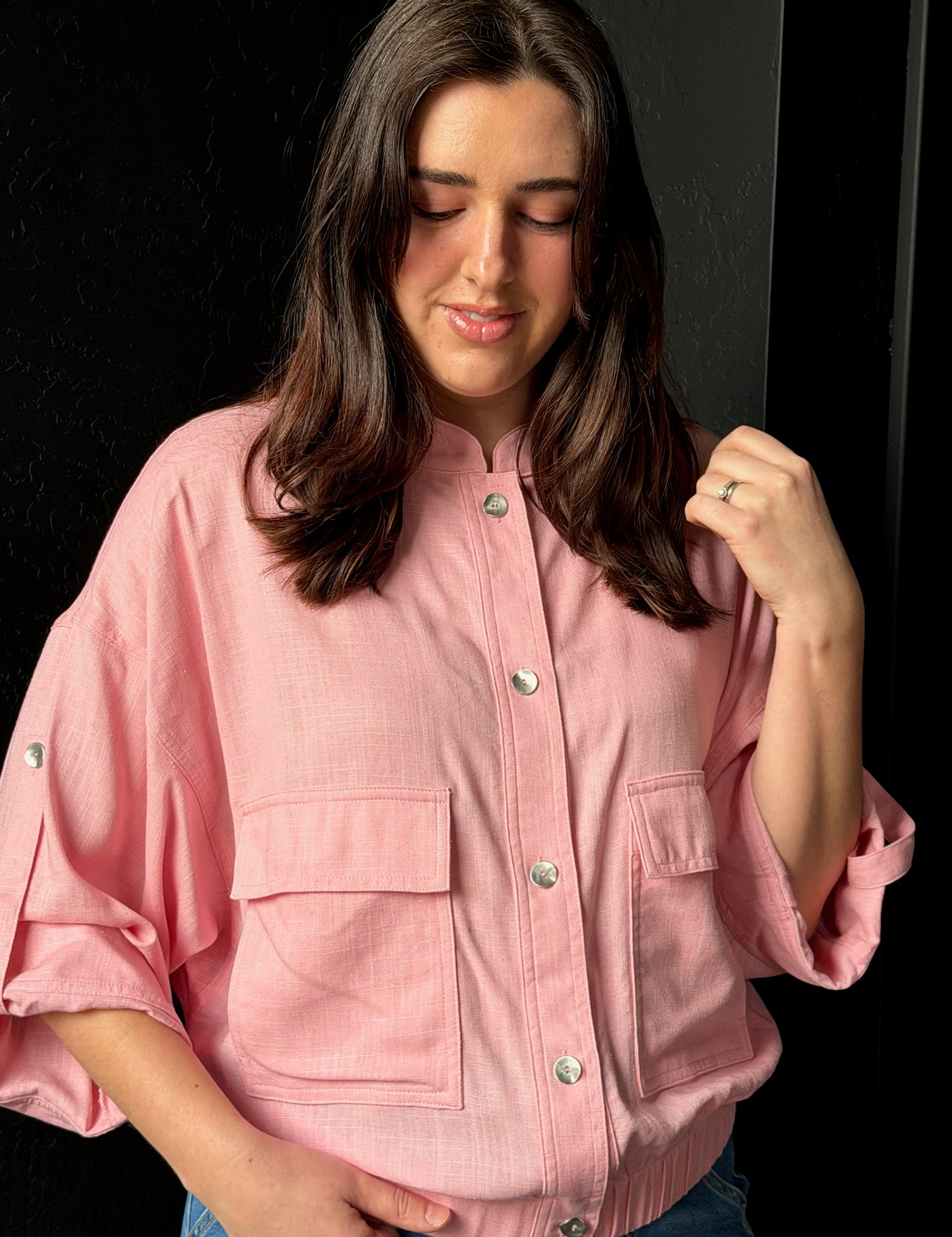 Woman wearing a pink jacket with button details against a black background