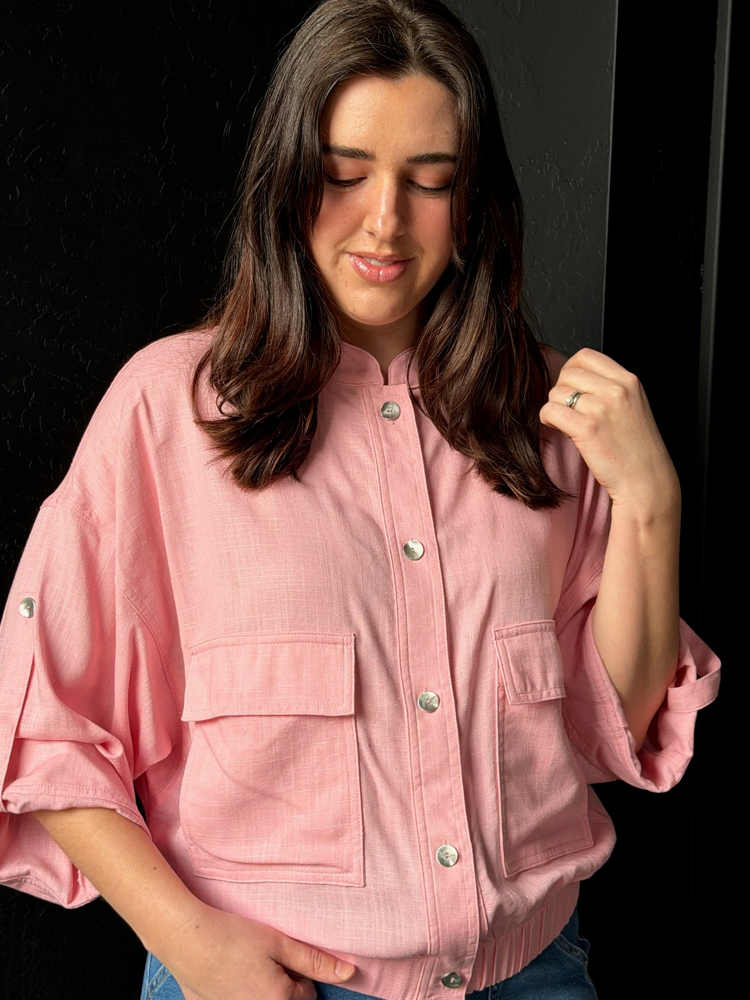 Woman wearing a pink jacket with button details against a black background
