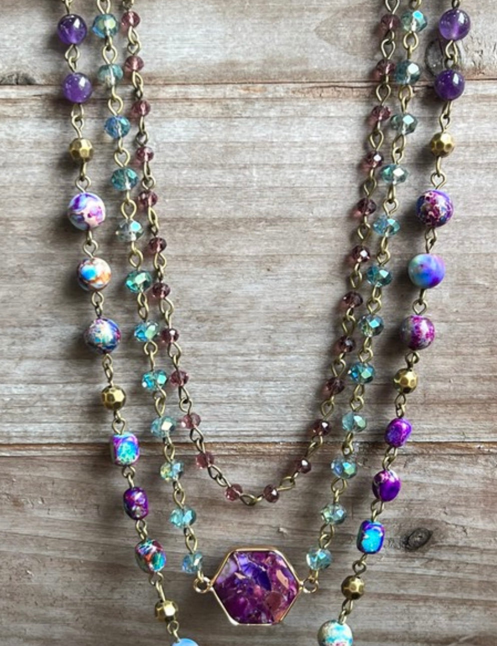 A multi-layered purple necklace with various beads and stones displayed on a wooden surface.