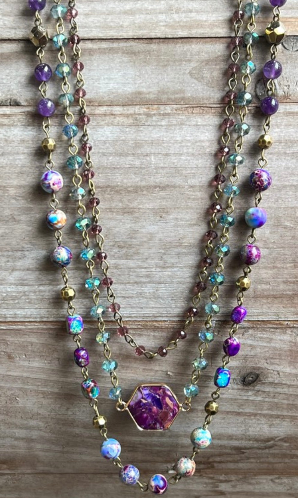 A multi-layered purple necklace with various beads and stones displayed on a wooden surface.