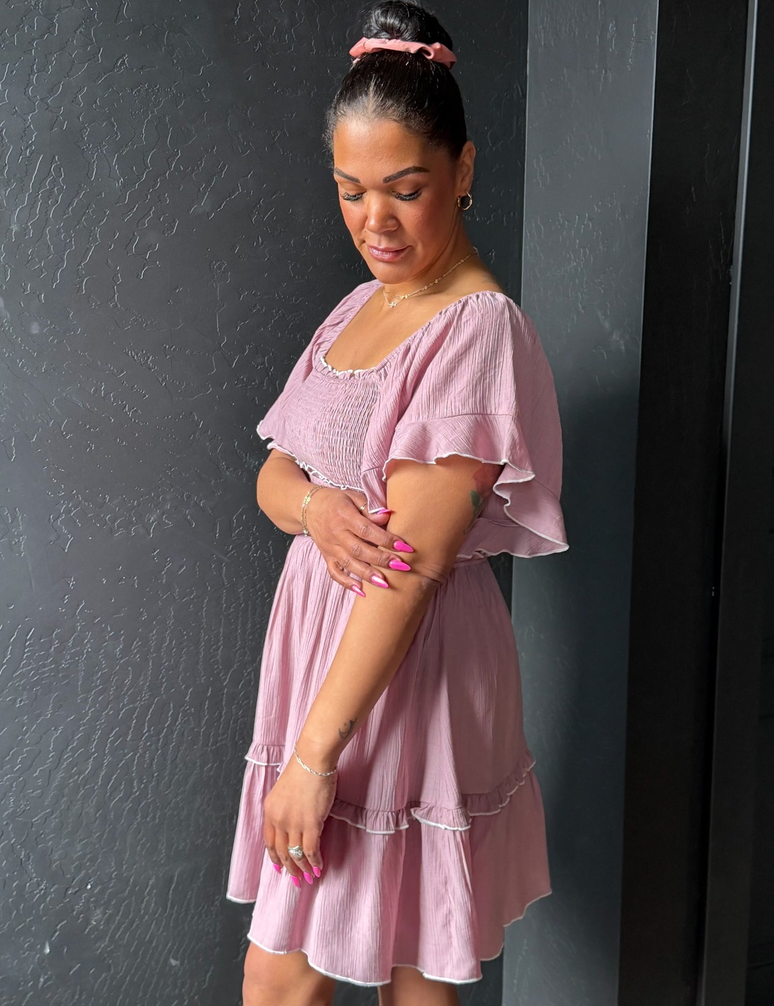 Woman wearing a pink dress against a dark gray wall
