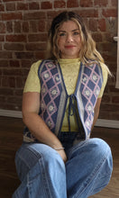 Woman wearing a patterned vest sitting against a brick wall.