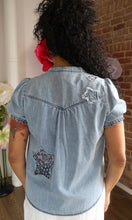 Person wearing a denim shirt with star designs in front of a brick wall.