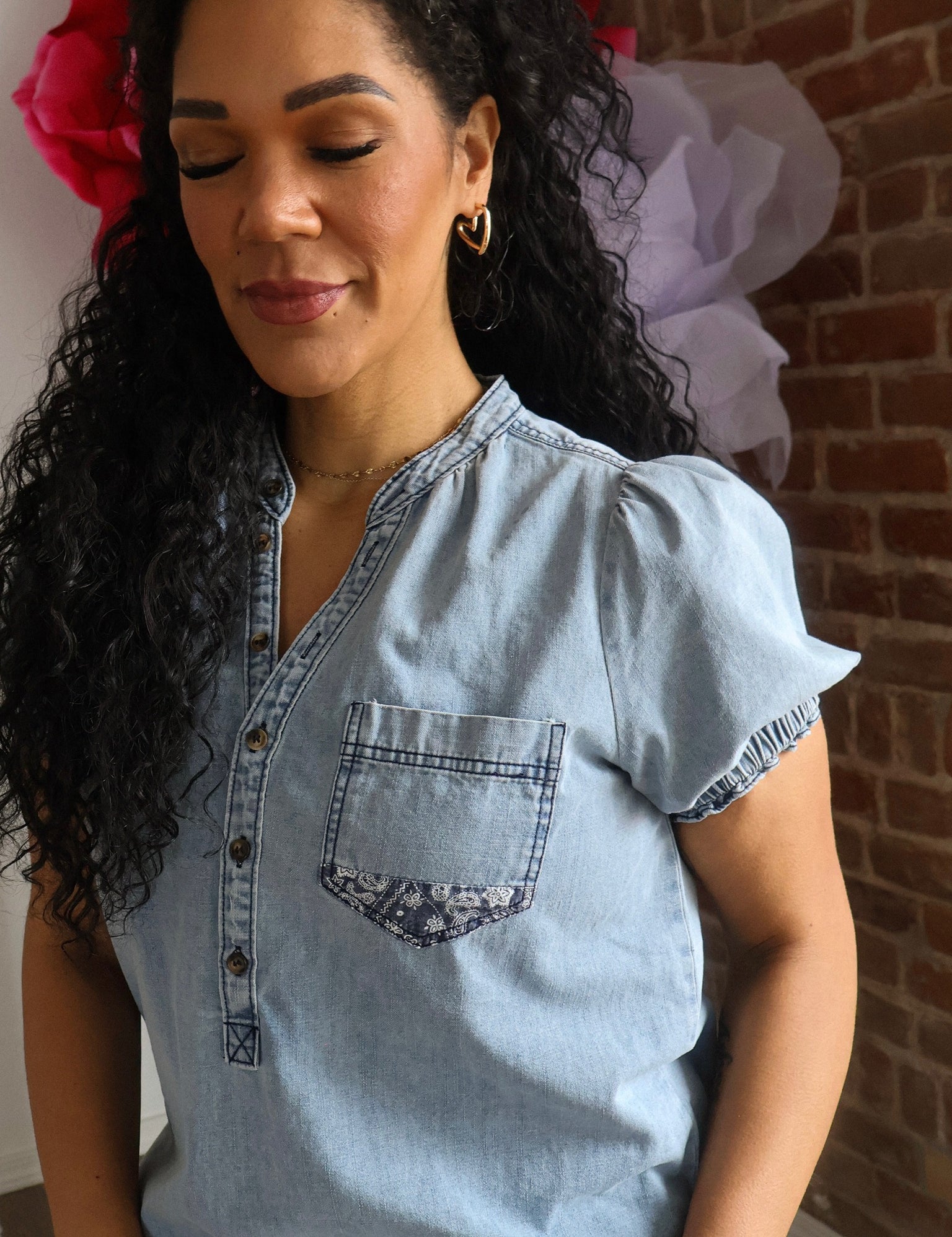 Woman wearing a light blue denim shirt with a brick wall background