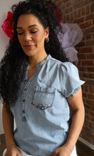 Woman wearing a light blue denim shirt with a brick wall background
