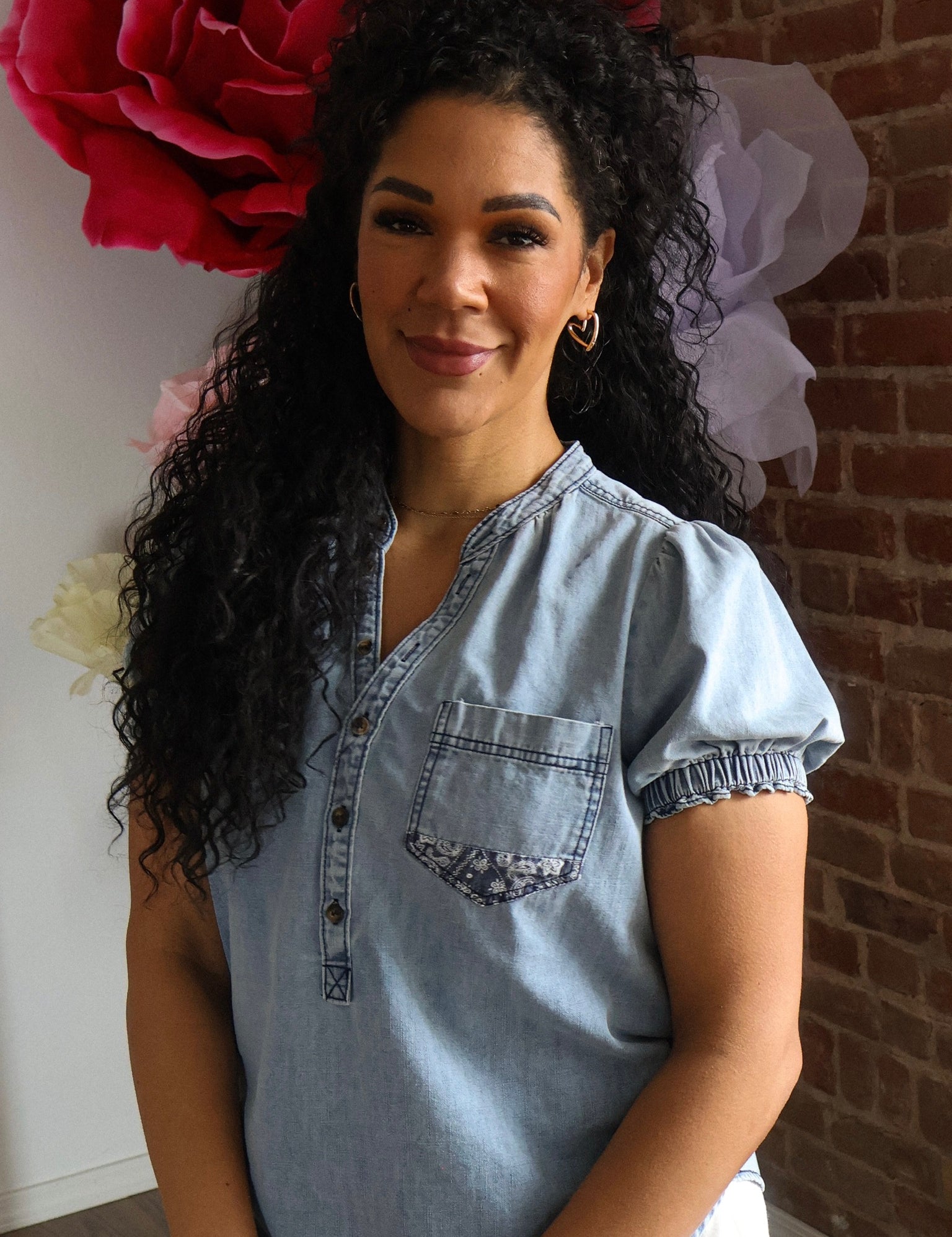 Woman wearing a denim shirt with a large red flower and white headpiece in the background.