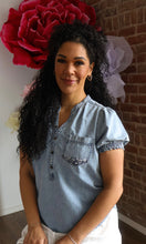 Woman wearing a denim shirt with a large red flower and white headpiece in the background.