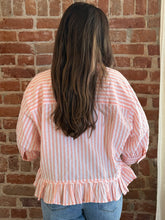 Person wearing a pink and white striped blouse with ruffled details against a brick wall.