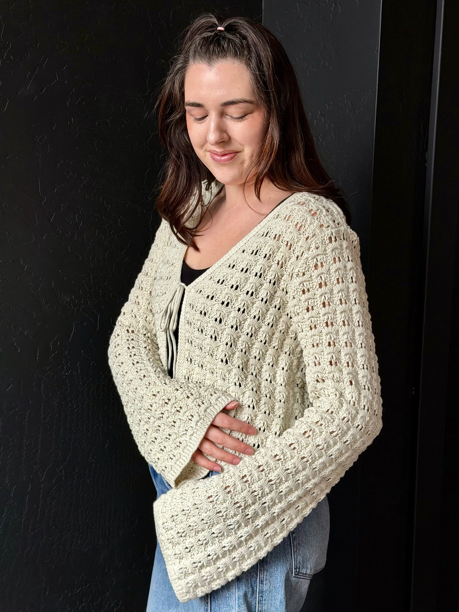 Woman wearing a cream-colored crochet poncho against a black background