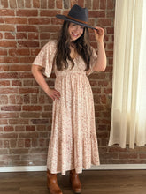 Woman wearing a floral dress and hat against a brick wall.