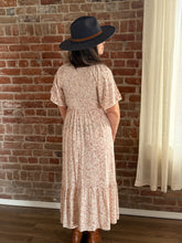 Person wearing a floral dress and dark hat against a brick wall.