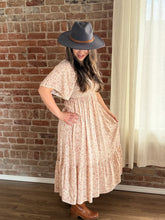Woman wearing a patterned dress and gray hat against a brick wall.