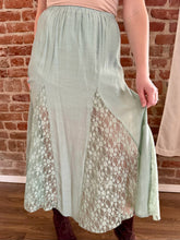 Person wearing a light green skirt with lace details in front of a brick wall.