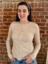 Woman wearing a beige long-sleeve shirt against a brick wall