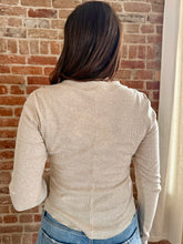 Person wearing a beige long-sleeve shirt against a brick wall.