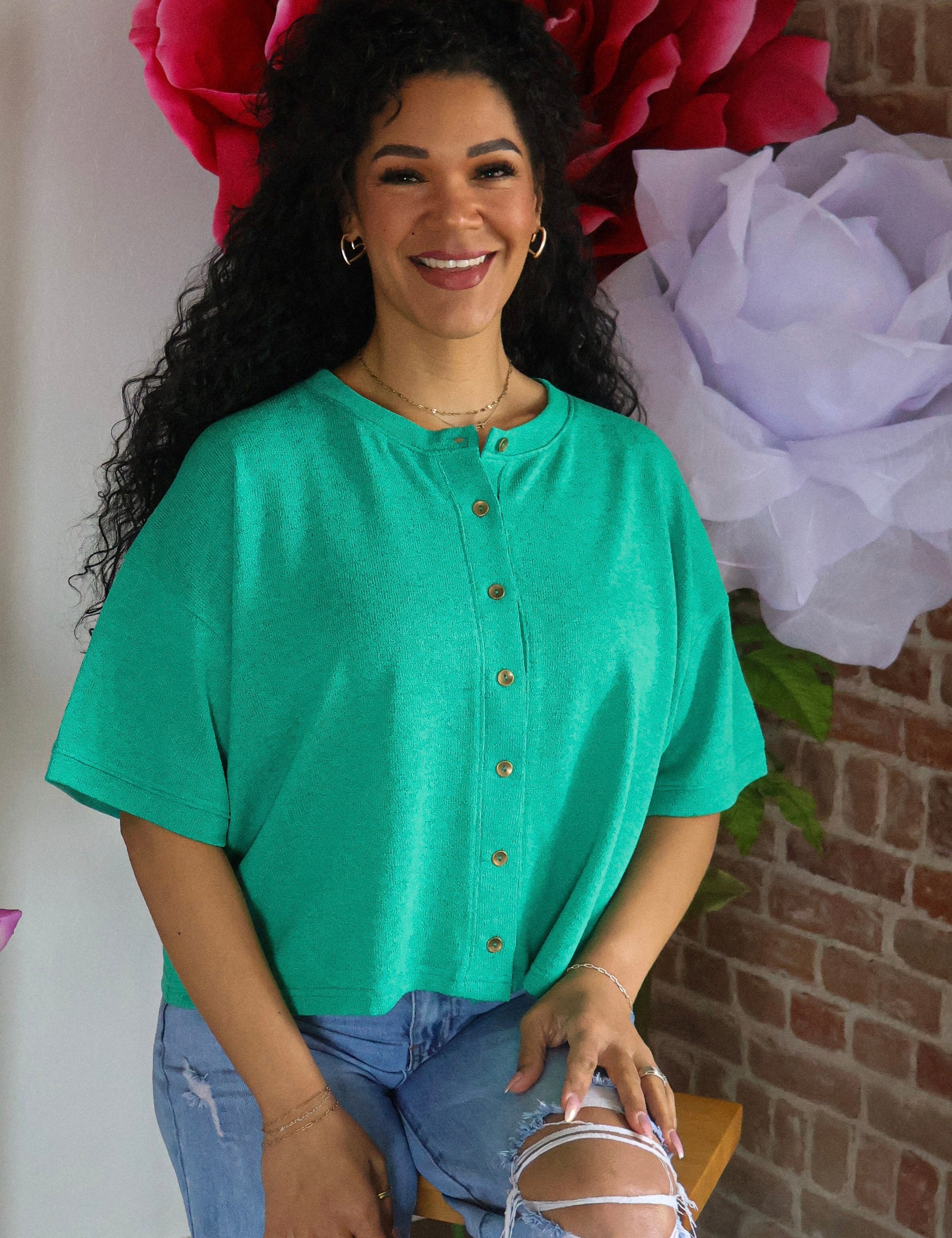 Woman in a green shirt sitting in front of large flowers with a brick wall background