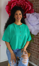Woman in a green shirt sitting in front of large flowers with a brick wall background