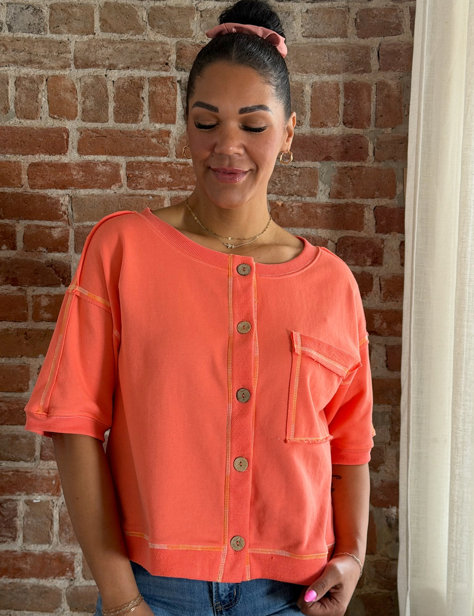 Woman wearing an orange button-up shirt against a brick wall